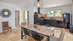 A modern kitchen with dark cabinetry, a large island, and a dining area with a wooden table and wicker chairs. - Nice home in Grignan with private swimming pool, can be inside or outside (Grignan)