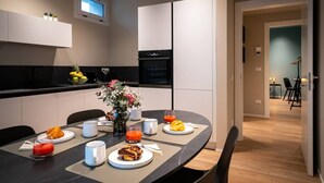 A modern kitchen with a dining area, featuring a round table with plates, cups, and a vase of flowers.