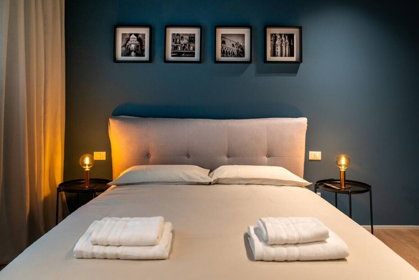 Une chambre à coucher avec un grand lit, deux tables de chevet avec des lampes et trois tableaux encadrés accrochés au mur.