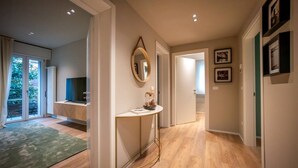 A hallway with wooden flooring, a round mirror, a small table with a vase, and a door leading to another room.