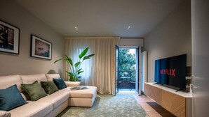 A modern living room with a sofa, a television, a plant, and a view to the outside.