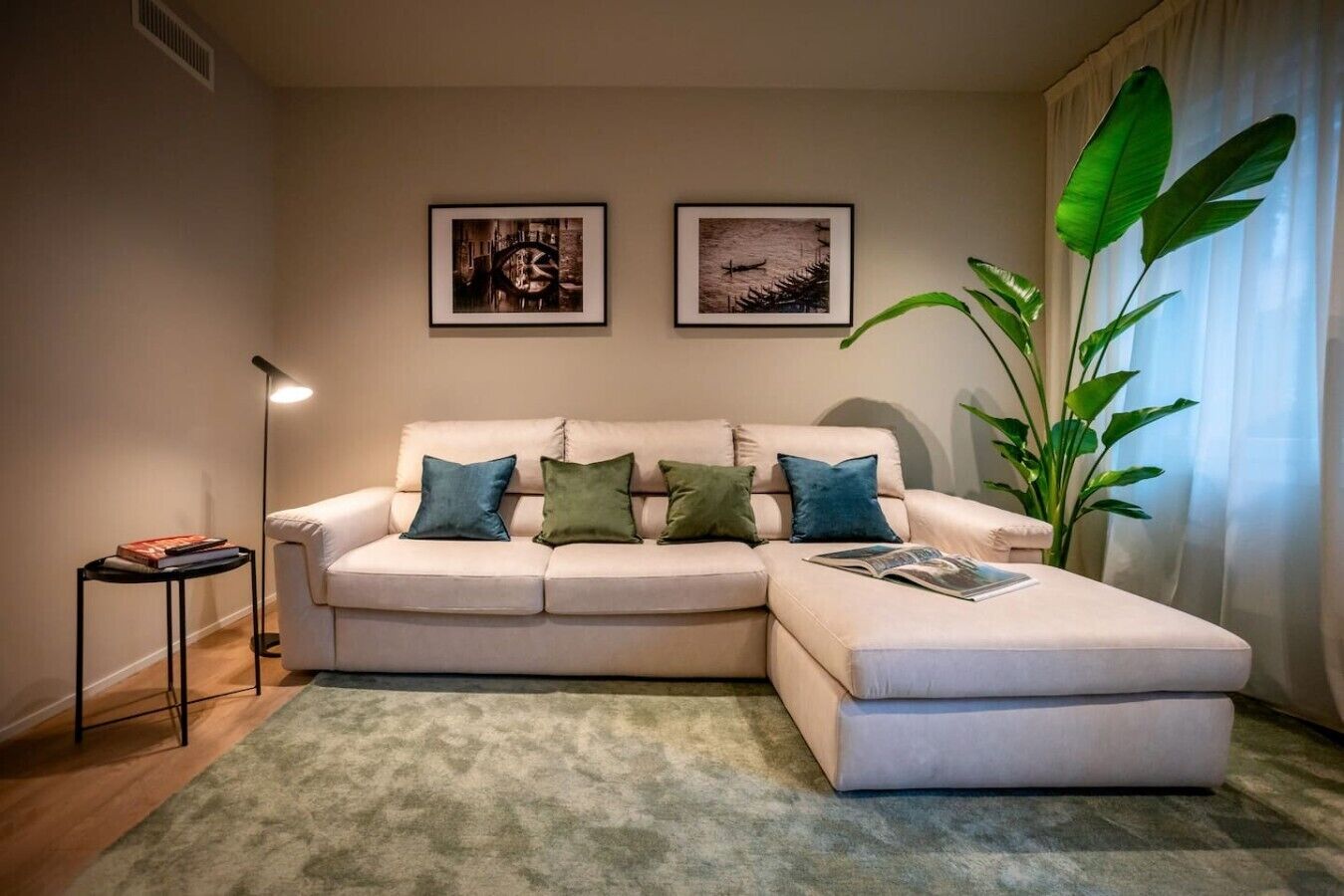 Un soggiorno con un divano color beige, un tavolino, una lampada da terra e due quadri appesi al muro.