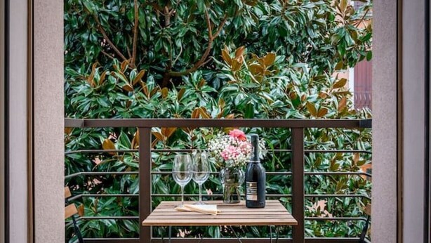 A balcony with a table set for two, a bottle of wine, and a vase of flowers.