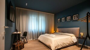 A bedroom with a bed, a desk, a chair, a suitcase, and a window with curtains.