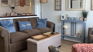 Una sala de estar con sofá, reposapiés y una consola con espejo y objetos decorativos.