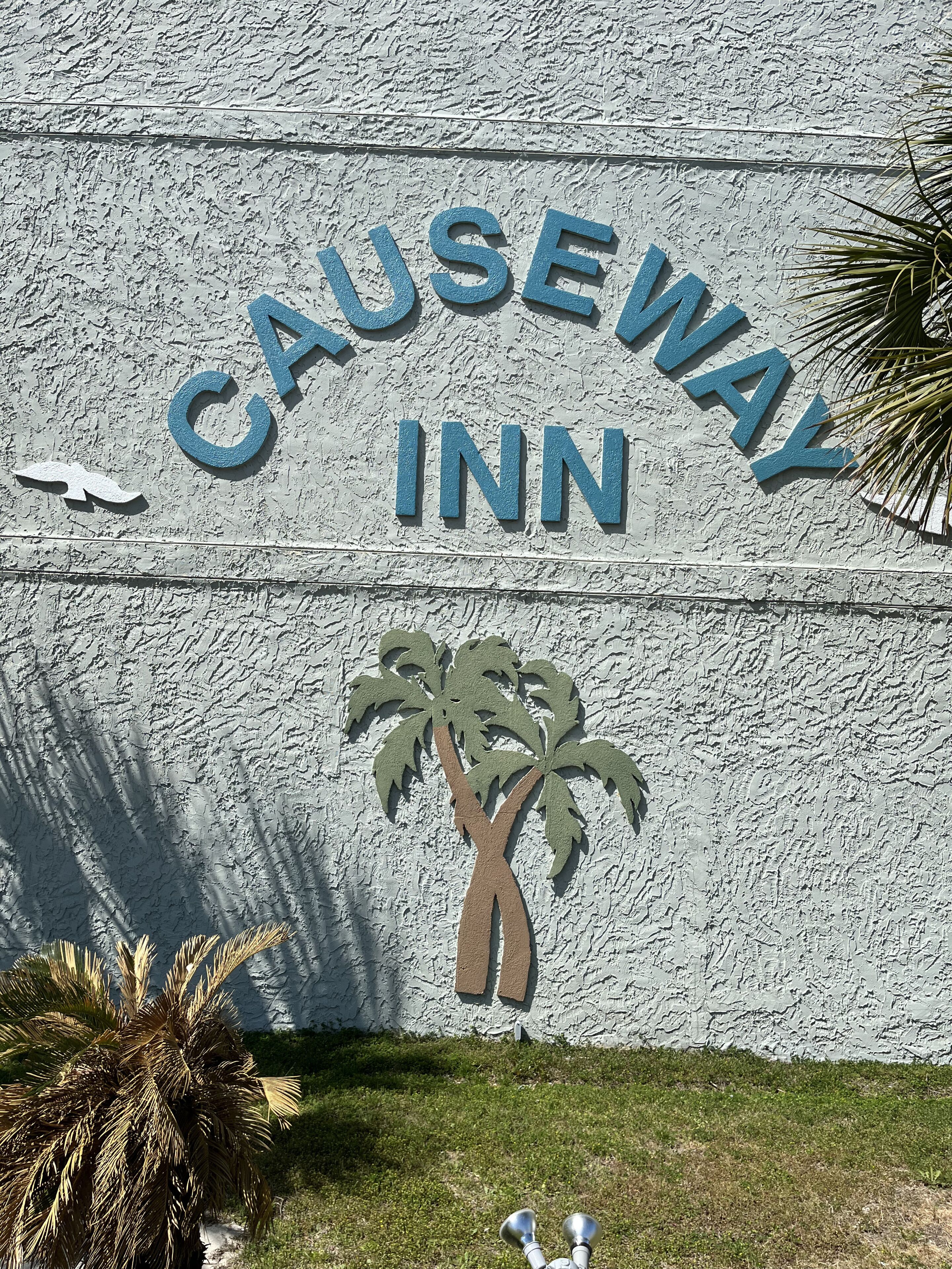 Eine Wand mit dem Schriftzug 'CAUSEWAY INN' und einer Grafik einer Palme.