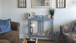Una sala de estar con un sofá, una mesa de centro, una consola con televisor y objetos decorativos.