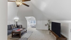 Een ruime loft met een hoge plafond, een plafondventilator, een grote flatscreen televisie, een bank, een salontafel en een potplant.