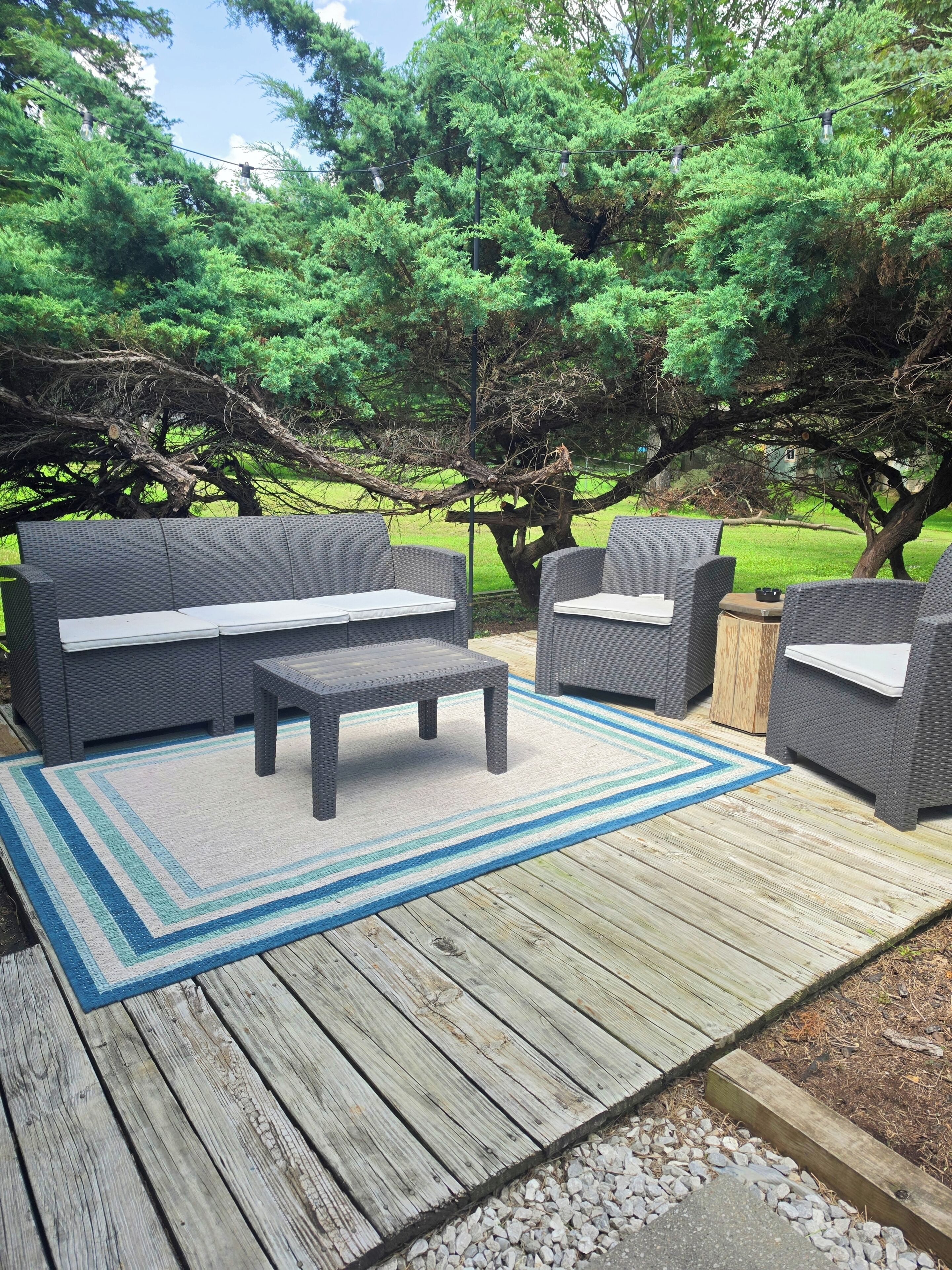 An outdoor patio with wicker furniture, a striped rug, and a wooden deck.