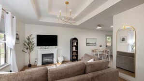 Ein Wohnzimmer mit Ecksofa, Kamin, Fernseher, Essbereich und Spiegel.
