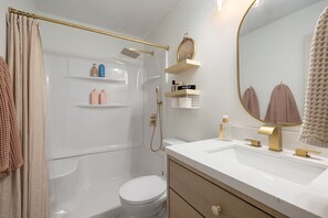 A modern bathroom with a glass shower enclosure, a white toilet, a vanity with a gold faucet, and a large mirror.