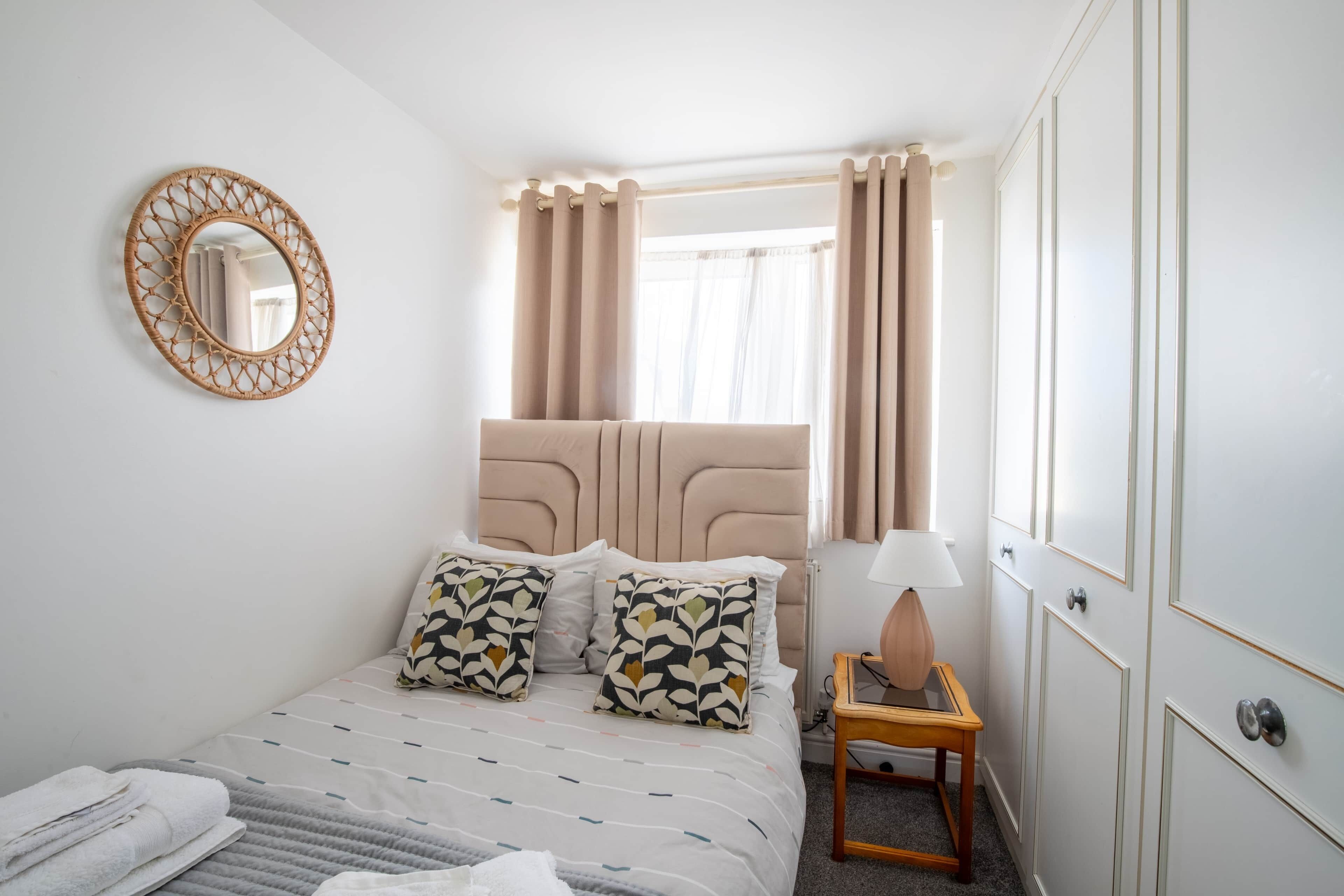 Une chambre d’hôtel comprenant un lit, une table de chevet avec une lampe, une armoire, une fenêtre avec des rideaux et un miroir fixé au mur.