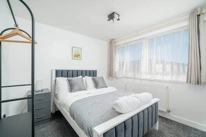 Een slaapkamer met een bed, een nachtkastje, een hanglamp, een radiator en een raam met gordijnen.