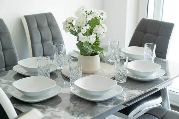 Une table à manger dressée avec de l’argenterie blanche, de la verrerie transparente et une plante en pot ornée de fleurs blanches.