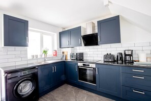 A modern kitchen with dark blue cabinets, a washing machine, a microwave, an oven, and a coffee maker.