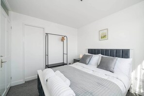 Une chambre à coucher avec un lit, une table de chevet, une étagère fixée au mur et une porte.