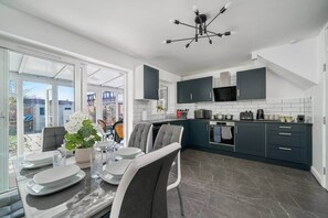 Eine moderne Küche mit dunklen Schränken, einer zentralen Kochinsel und einem Essbereich mit Tisch für vier Personen.