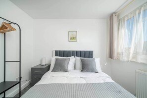 Ein ordentlich eingerichtetes Schlafzimmer mit Bett, Nachttisch und Kleiderstange.