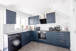 Een moderne keuken met donkerblauwe kastjes, een inbouwoven, een magnetron en een wasmachine.