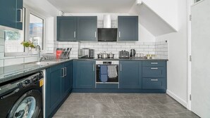 Een kleine keuken met donkerblauwe kastjes, een ingebouwde magnetron en een vaatwasser.
