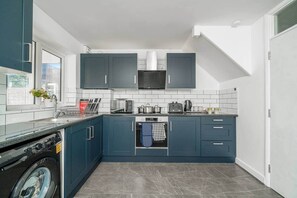Une cuisine compacte avec des meubles de couleur bleu foncé, un four à micro-ondes encastré et un lave-vaisselle.