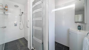 Een moderne badkamer met een douchecabine van glas, een handdoekhouder, een wastafel met spiegel en een kast.