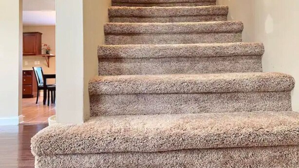 Una escalera alfombrada con barandilla, que sube a un piso superior.