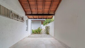 Un estrecho pasillo con suelo de baldosas, techo de madera y pared blanca con una ventana.