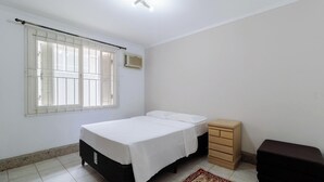 Un dormitorio con cama, cómoda, ventana con persianas y una lámpara en el techo.