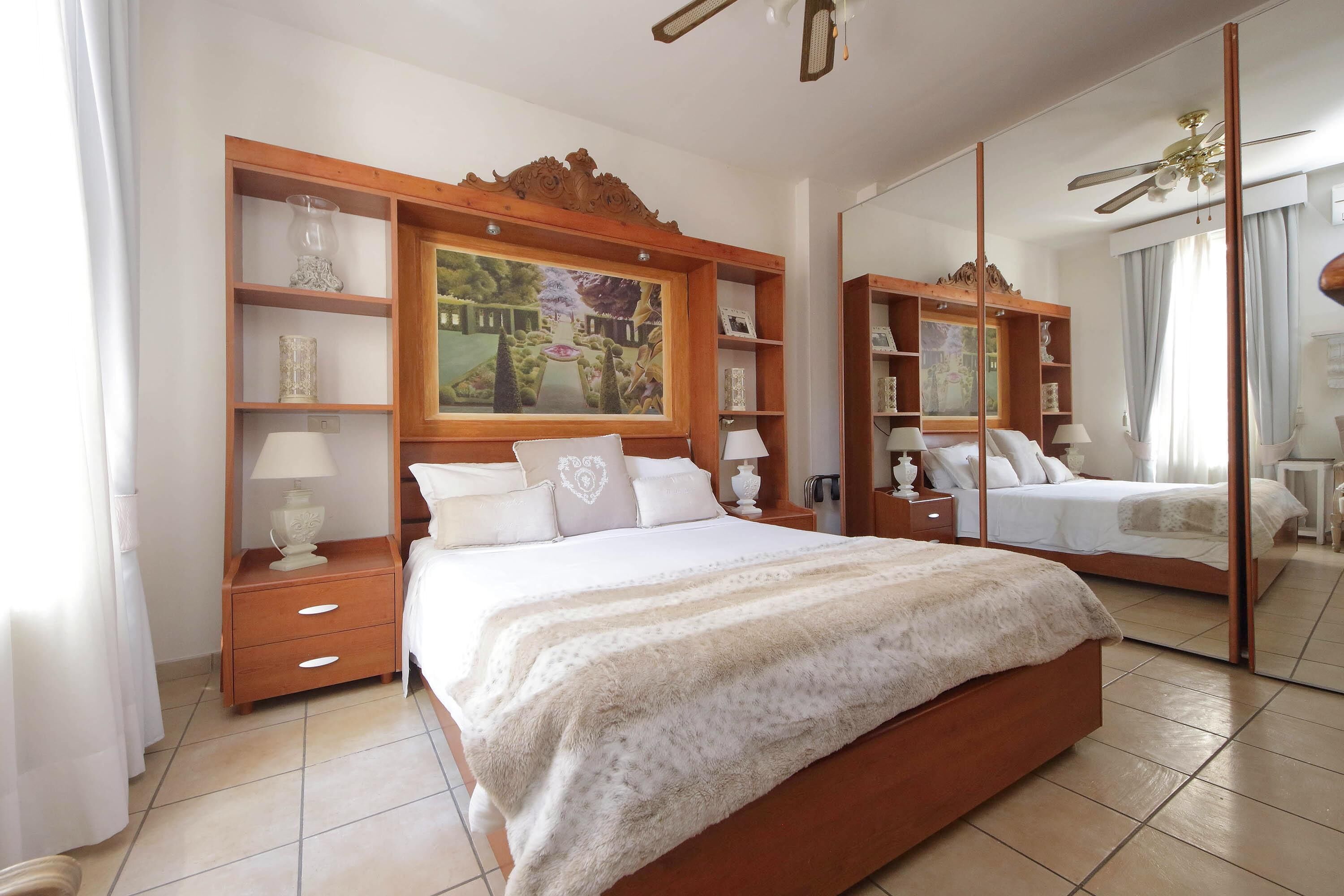 A spacious bedroom with a large bed, wooden headboard, bedside tables, and a mirror.