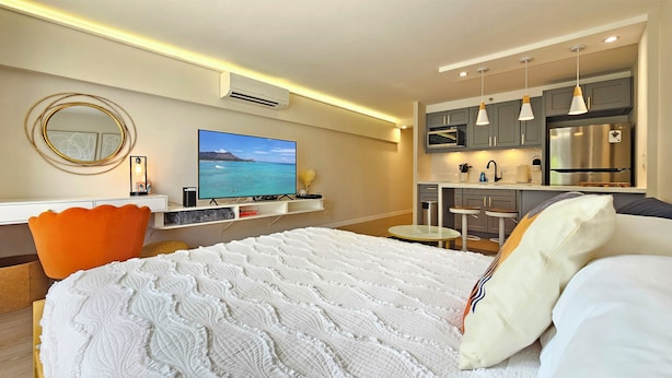 A modern hotel room with a bed, a desk, a TV, and a kitchenette. - Stunning Studio w/Pool & Includes Free Dedicated Parking Space (Honolulu)