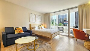 A hotel room with a bed, a sofa, a small table, a chair, and a balcony with a view of the city. - Stunning Studio w/Pool & Includes Free Dedicated Parking Space (Honolulu)