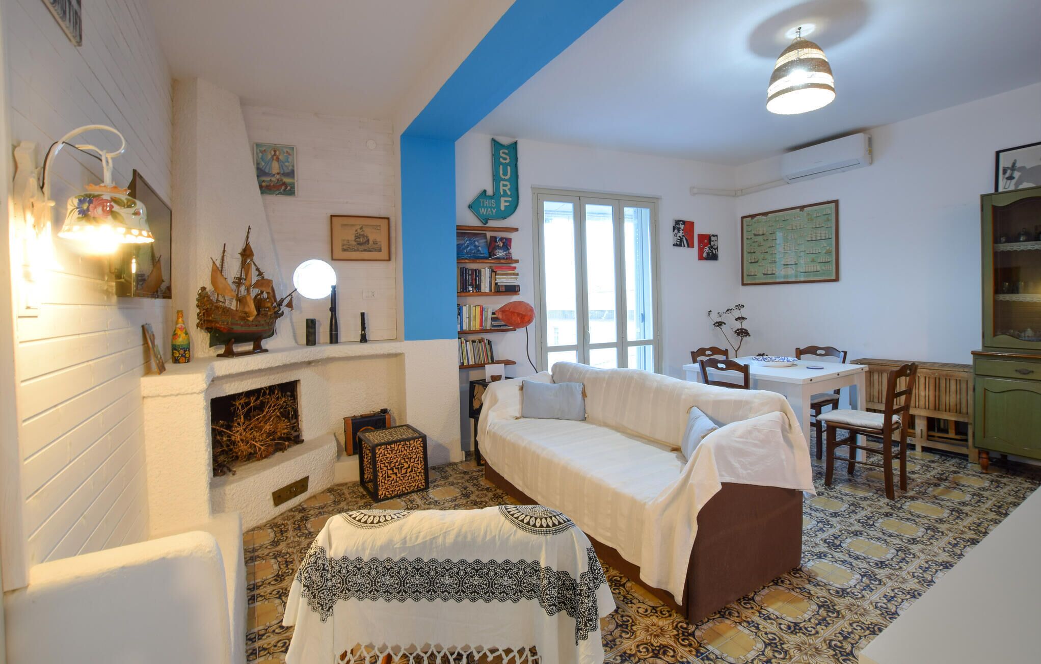 A cozy living room with a fireplace, a sofa, a dining table with chairs, and a bookshelf.