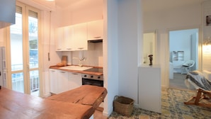 A compact kitchen with white cabinets, a wooden countertop, and a sink. There's a wicker basket on the floor and a small table with a chair. - 2 bedroom cozy apartment in Staletti (Staletti)