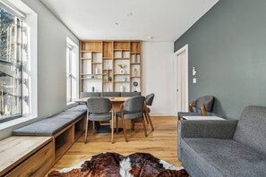 Ein modernes Wohnzimmer mit eingebautem Sitzbank, einer Essecke mit Holztisch und -stühlen sowie einem grauen Sofa.