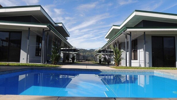 Un hôtel moderne doté d’une piscine, de bâtiments à deux étages et offrant une vue sur des collines en arrière-plan.