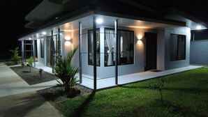 Une maison moderne à deux étages, dotée de grandes fenêtres et d’un éclairage extérieur soigné pour la nuit.
