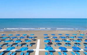 Una spiaggia con file di ombrelloni blu e lettini, un cielo sereno e l'oceano sullo sfondo.