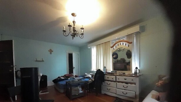 Una habitación con piso de madera, un candelabro, una cama, un aparador y un espejo.