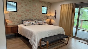 Una camera da letto con un letto, comodini, una panca, una ventola a soffitto e vista sull'esterno.