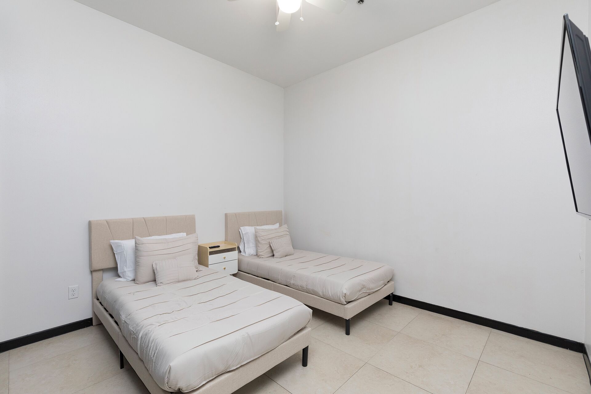 A small, clean room with two single beds, a nightstand, and a ceiling fan.