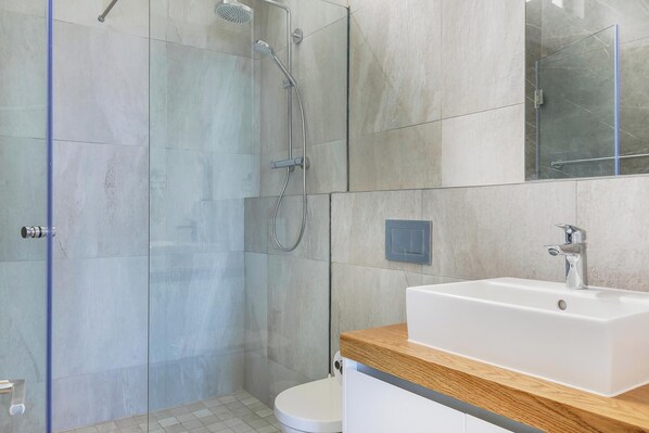 A modern bathroom with a glass shower enclosure, a white sink, and a wooden countertop. - Incredible Luxury Villa w Ocean Vistas The Views (Cape Town)