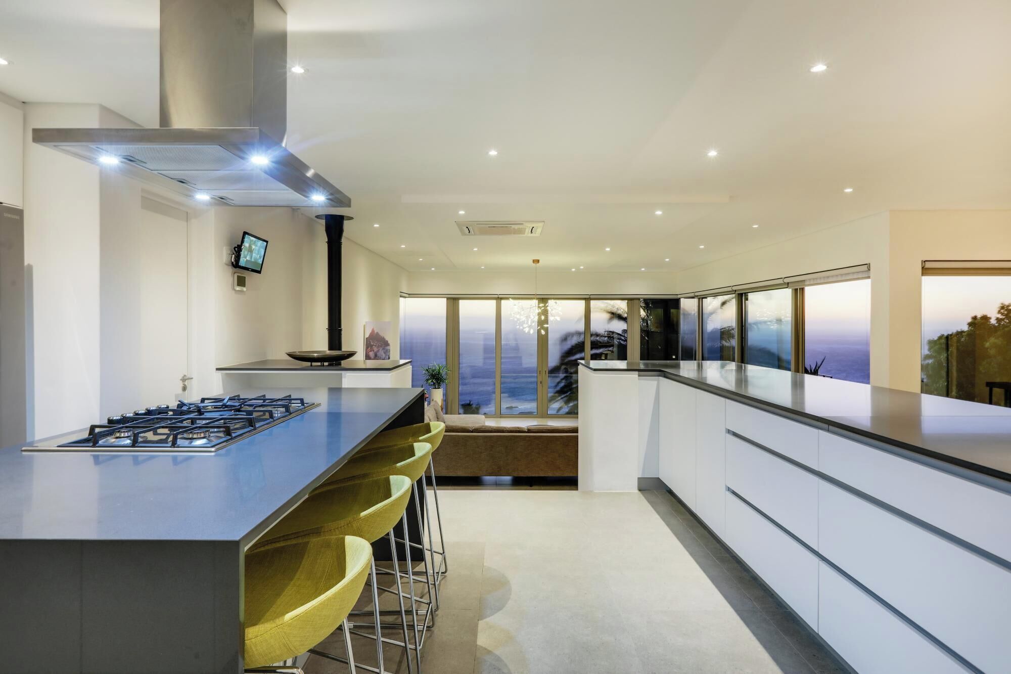 Una cocina moderna con una isla central, taburetes de bar, una estufa y un amplio ventanal con vistas.