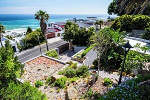 Una propiedad costera con vistas al océano, un camino de entrada pavimentado y un jardín con plantas variadas y un bebedero para pájaros.