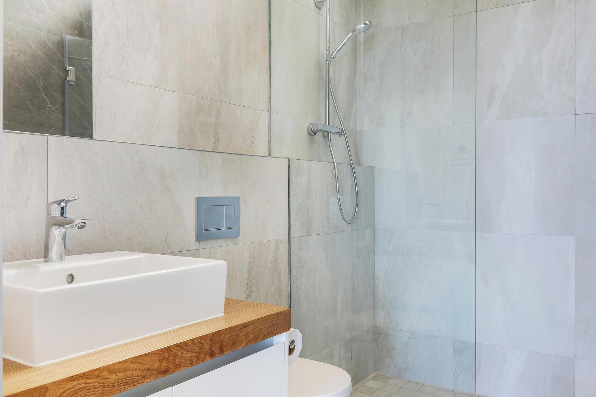 A modern bathroom with a white sink, wooden countertop, and a shower with a handheld showerhead.