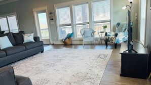Ein Wohnzimmer mit grauem Sofa, weißem Teppich, Korbsessel und einem Fernsehschrank.
