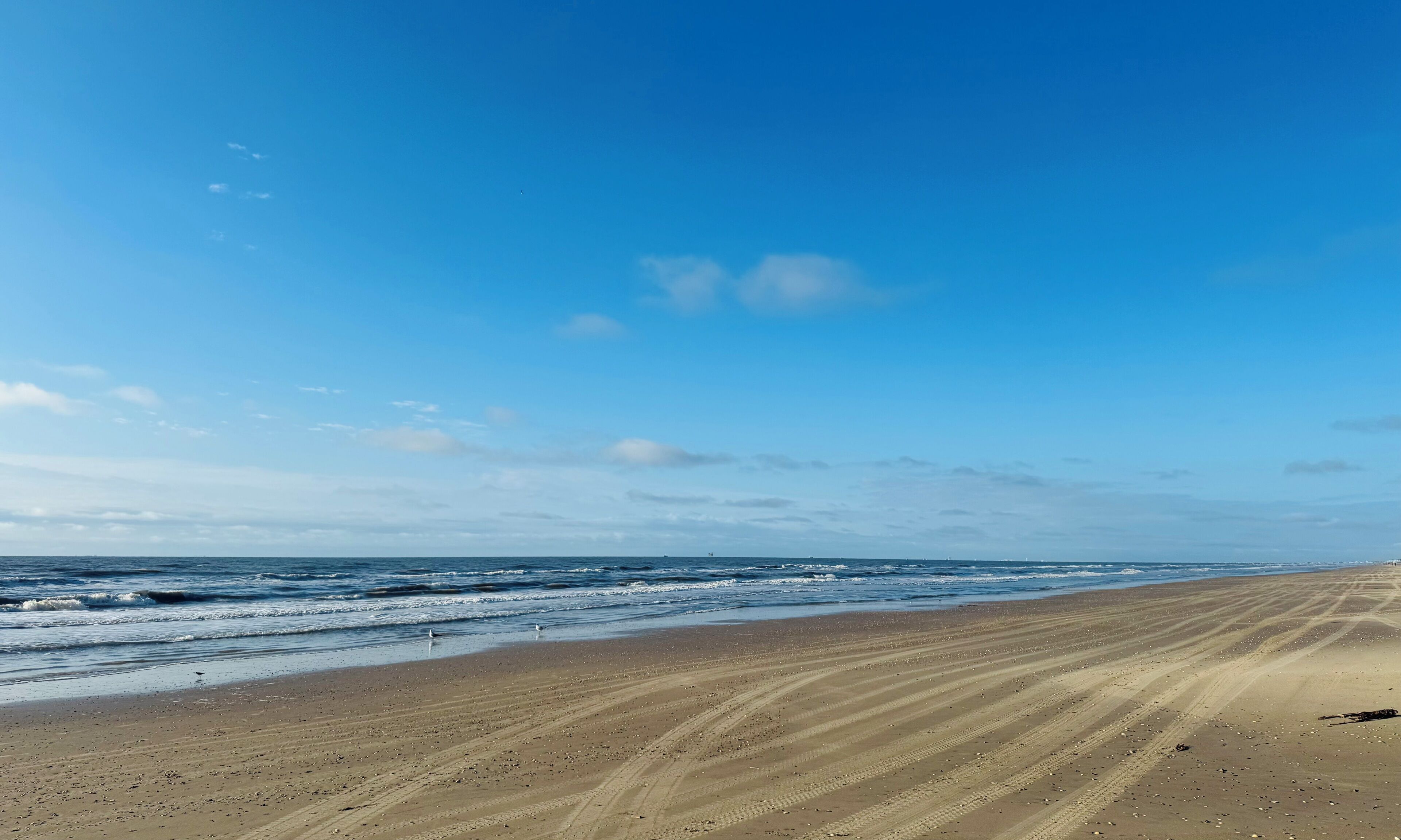 A wide sandy beach with gentle waves and a clear blue sky.