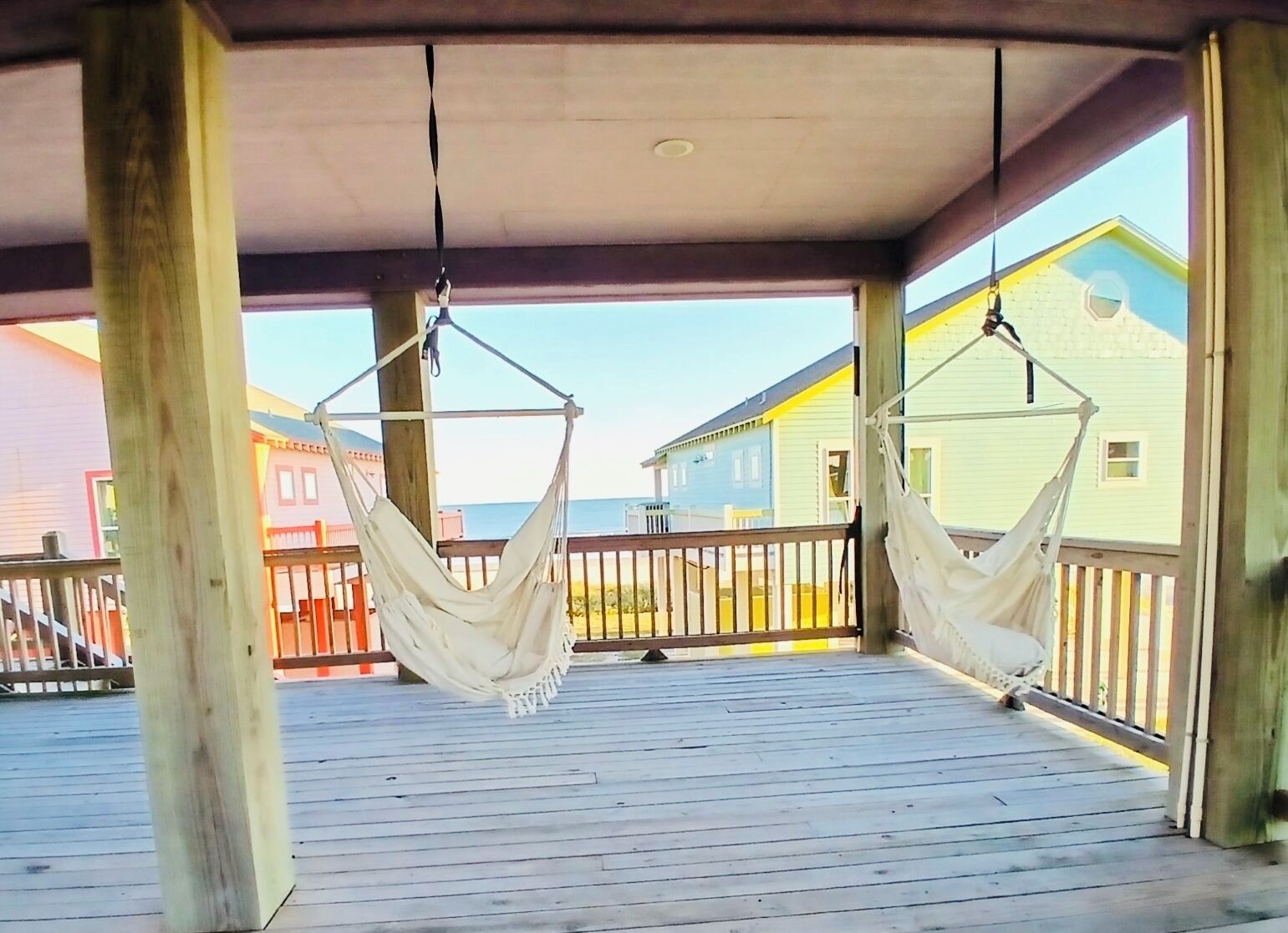 A wooden deck with two white hammocks suspended from the ceiling.