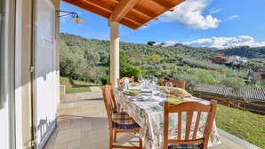 Un coin repas avec une table dressée pour quatre personnes, offrant une vue panoramique sur une colline verdoyante.