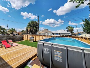 Ein oberirdischer Pool mit Holzterrasse, Liegestühlen und Grill.